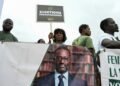 A supporter of the Coalition for a Peaceful Alternation holds a placard next to a political banner depicting the president of the Democratic Party of Ivory Coast (PDCI) Tidjane Thiam during their first meeting in Abidjan on May 31, 2025, ahead of the presidential election on October 25, 2025.
