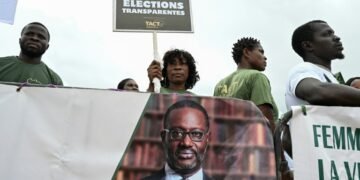 A supporter of the Coalition for a Peaceful Alternation holds a placard next to a political banner depicting the president of the Democratic Party of Ivory Coast (PDCI) Tidjane Thiam during their first meeting in Abidjan on May 31, 2025, ahead of the presidential election on October 25, 2025.