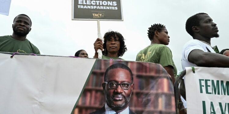 A supporter of the Coalition for a Peaceful Alternation holds a placard next to a political banner depicting the president of the Democratic Party of Ivory Coast (PDCI) Tidjane Thiam during their first meeting in Abidjan on May 31, 2025, ahead of the presidential election on October 25, 2025.